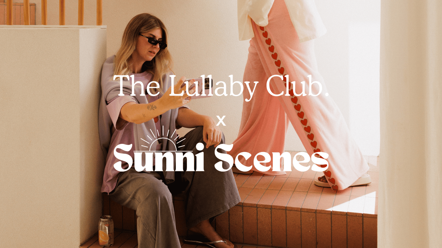 TLC x Sunni Scenes campaign image two women styled in the collection sitting and standing in a warm toned house location wearing the Darcy Knit Bomber and Essentials Pant in Love Story