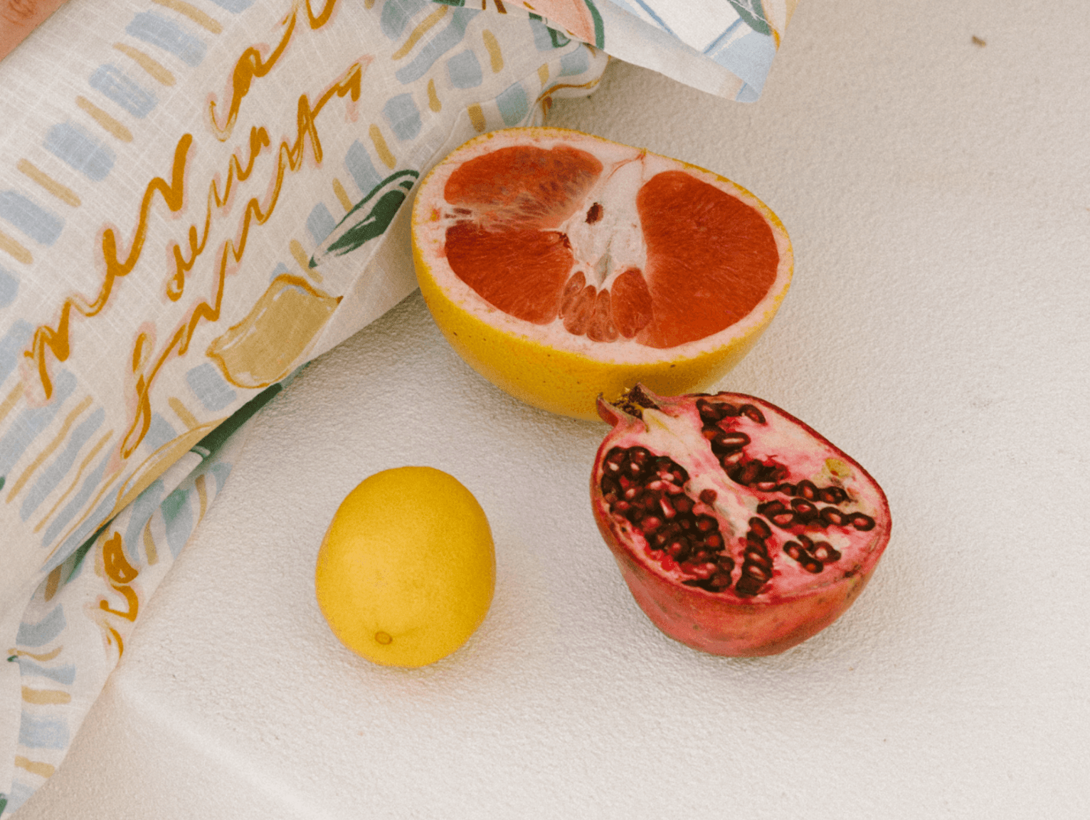 An arrangement of fruit including a lemon, pomegranate, grapefruit, while a printed pants in showing