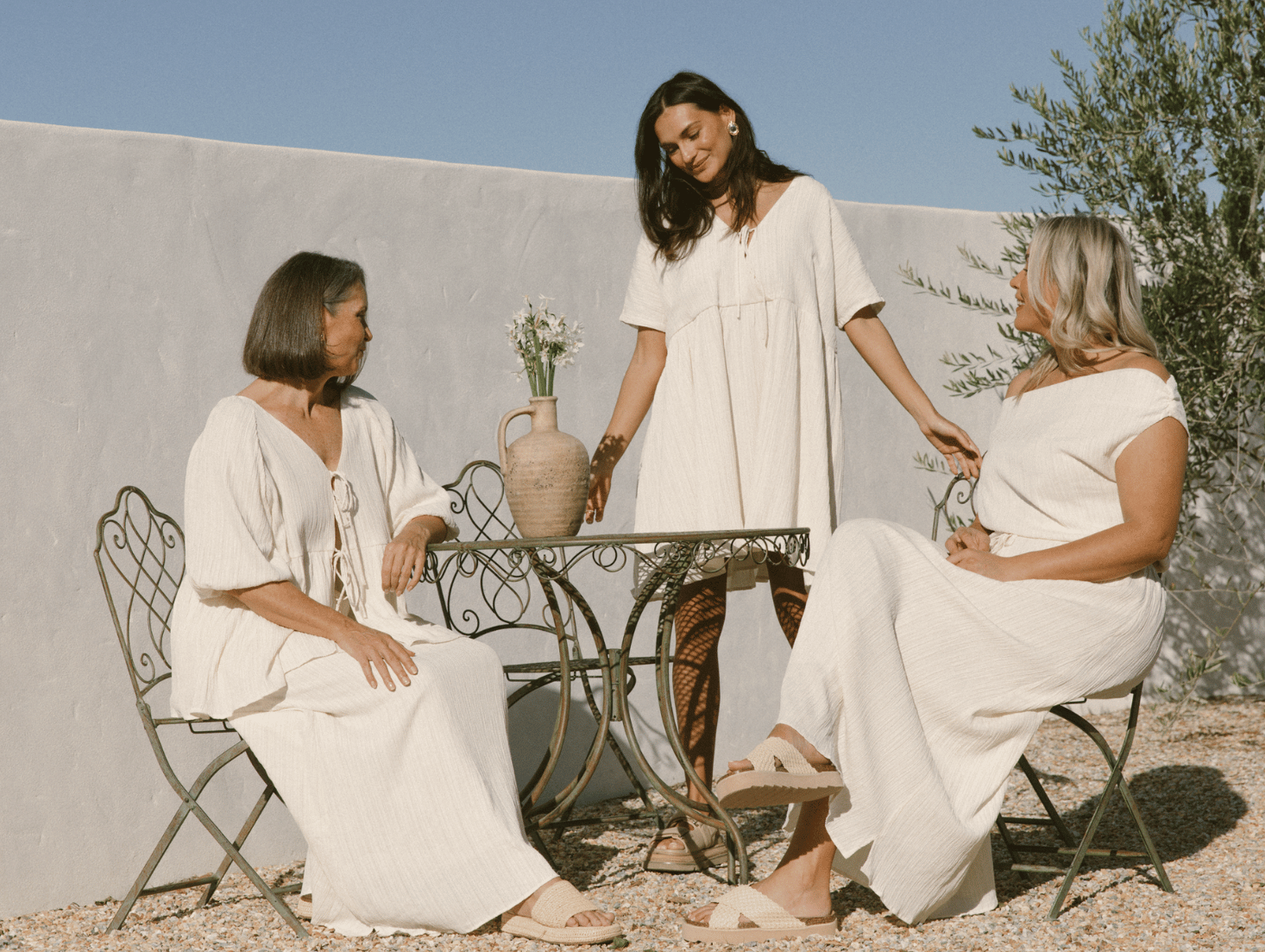 Models wearing garden breeze cream crepe dress skirt top in garden blue sunny skies greece euro summer aesthetic