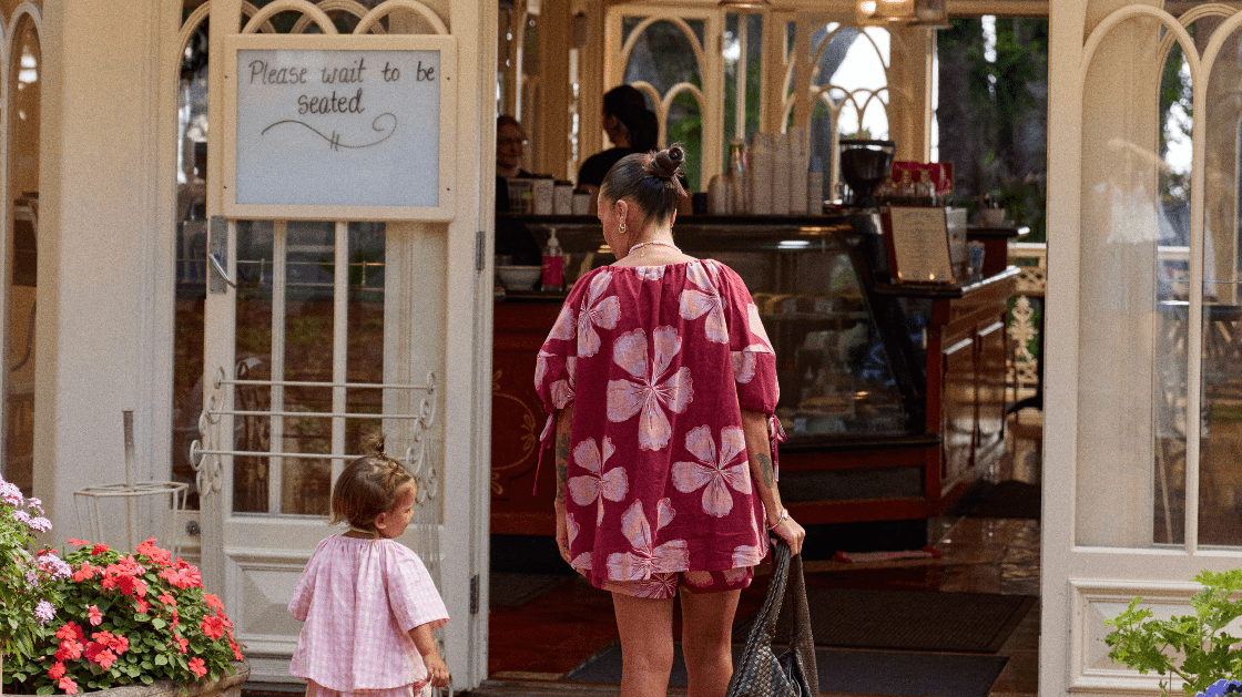 Women in maroon coloured set walking into a cafe with her toddler