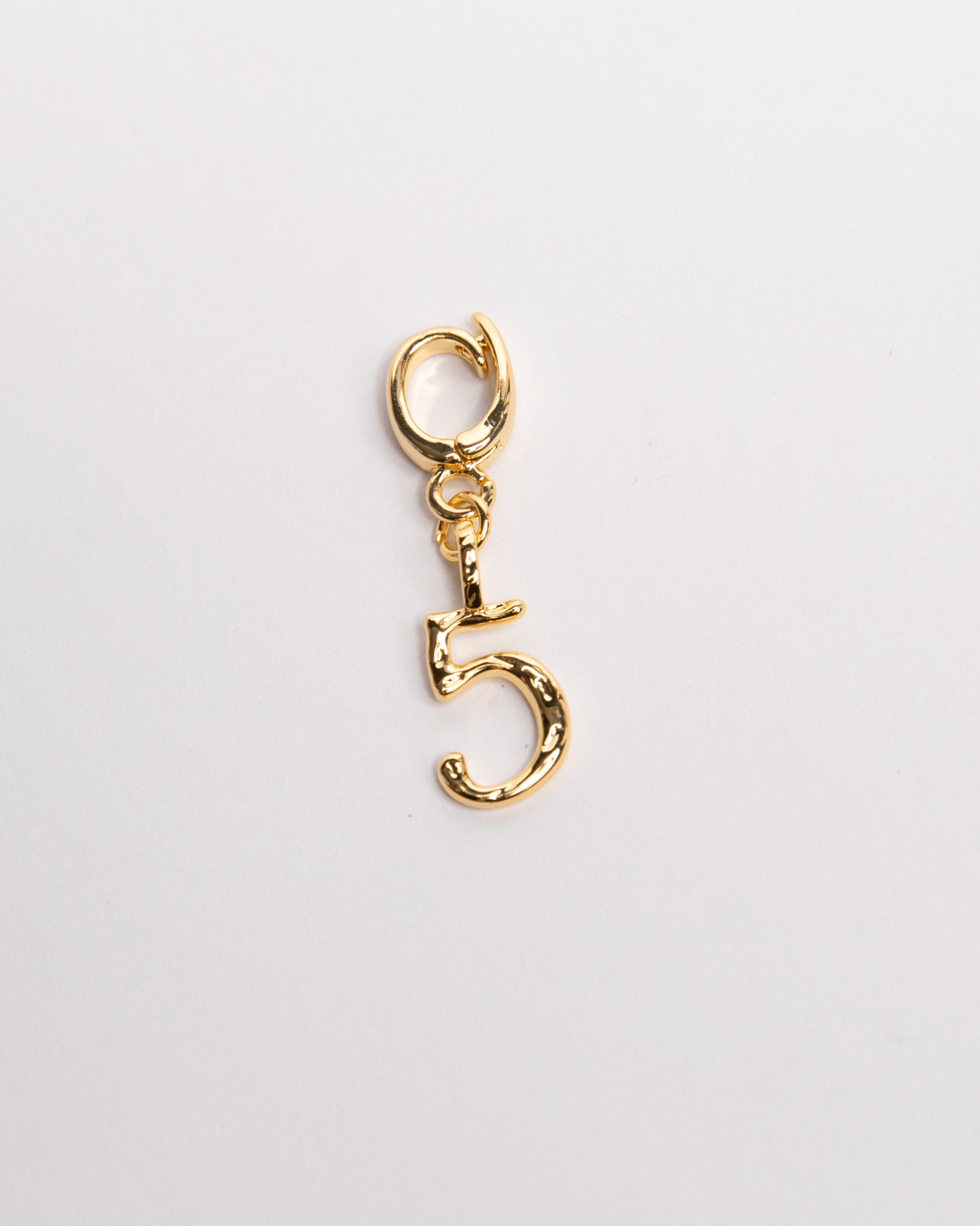 A gold-colored charm in the shape of the number 5 with a secure clasp, designed for attachment to jewelry such as necklaces and bracelets.
