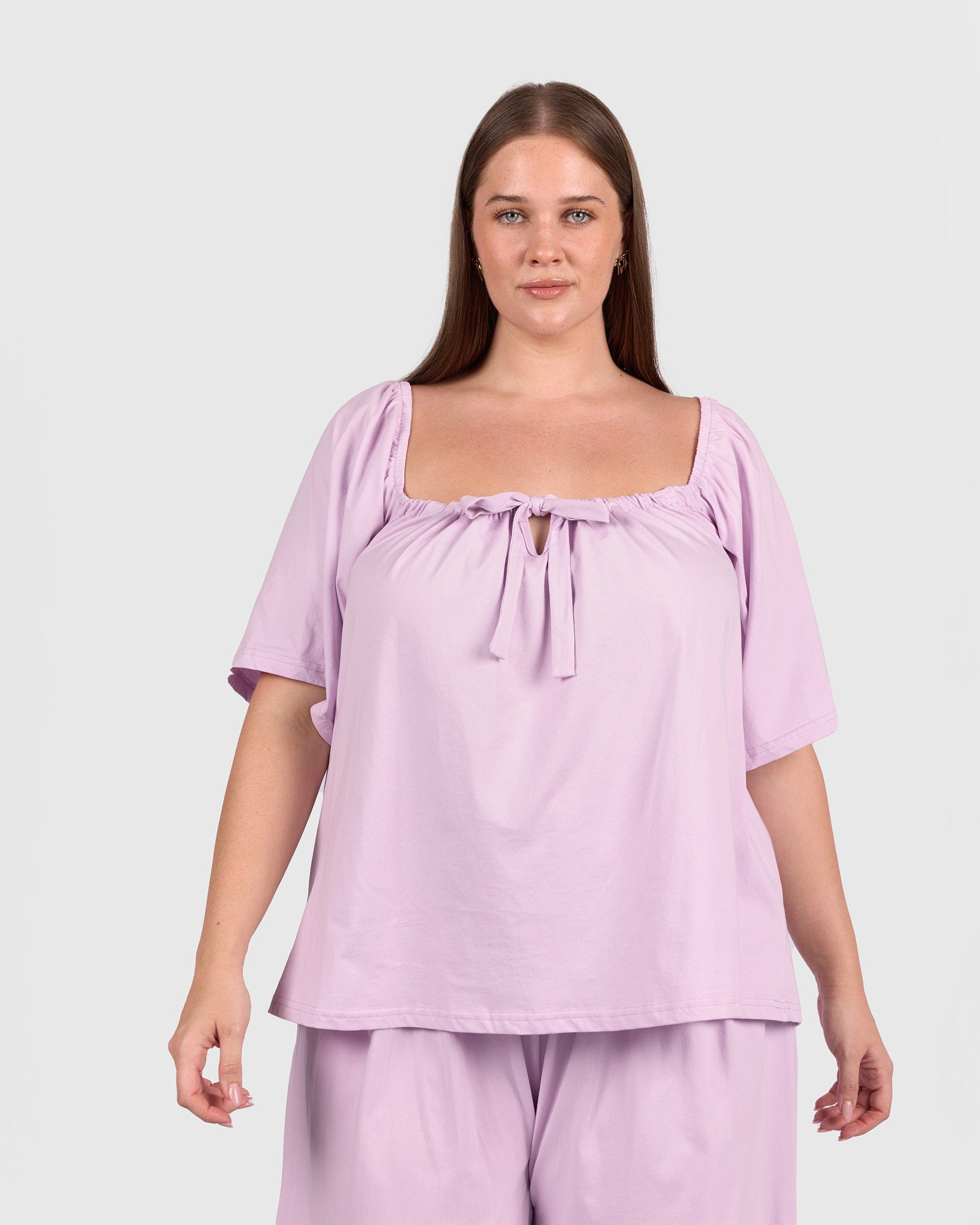 Woman wearing a light purple top and pants on a plain background