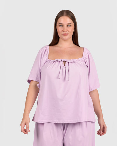 Woman wearing a light purple top and pants on a plain background