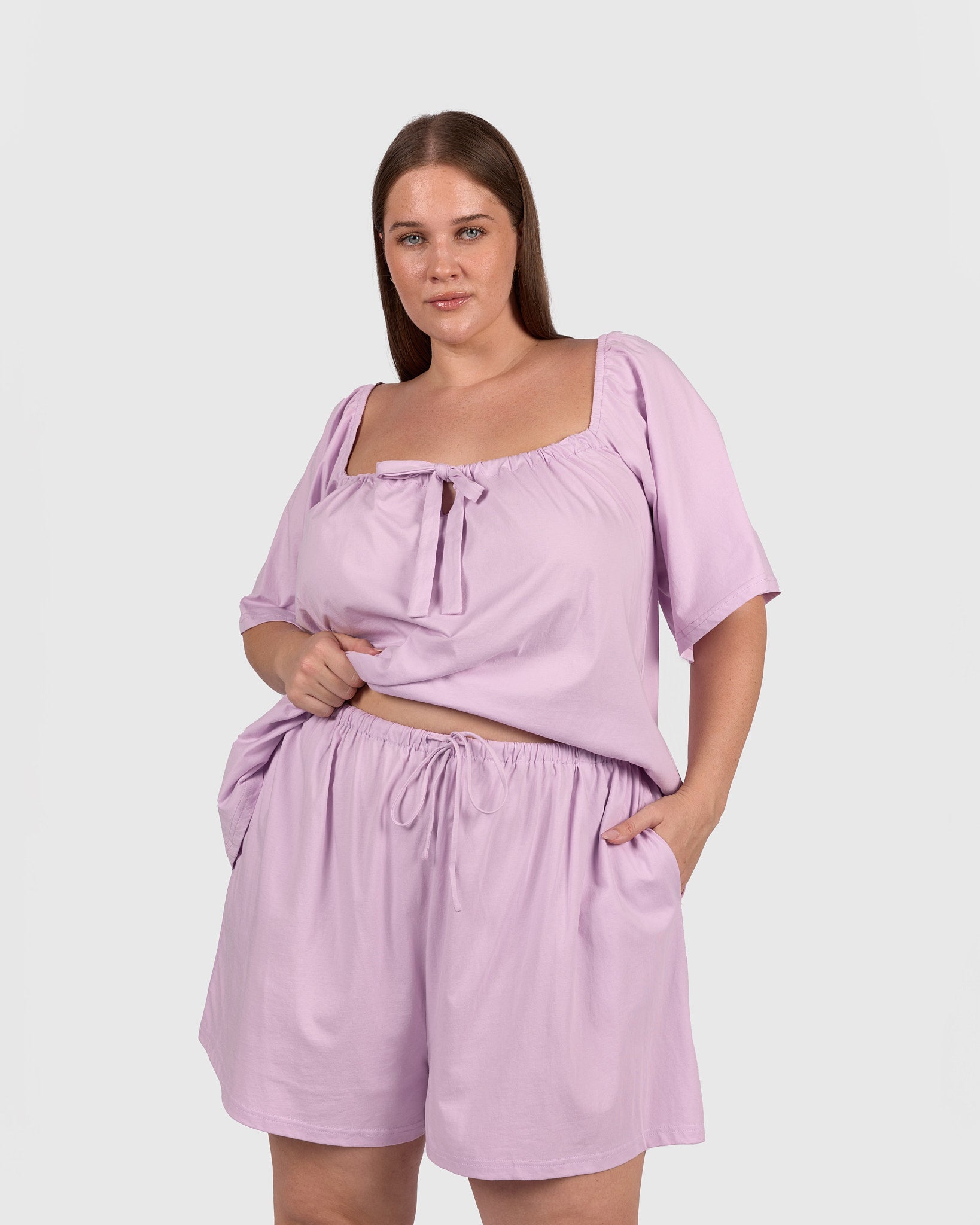 Woman wearing a light purple outfit with a top and shorts on a white background