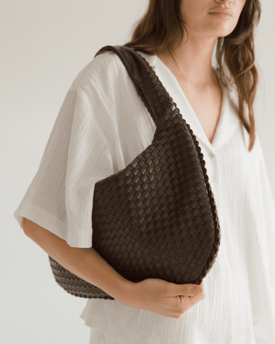 Woman holding a brown woven handbag against a plain background