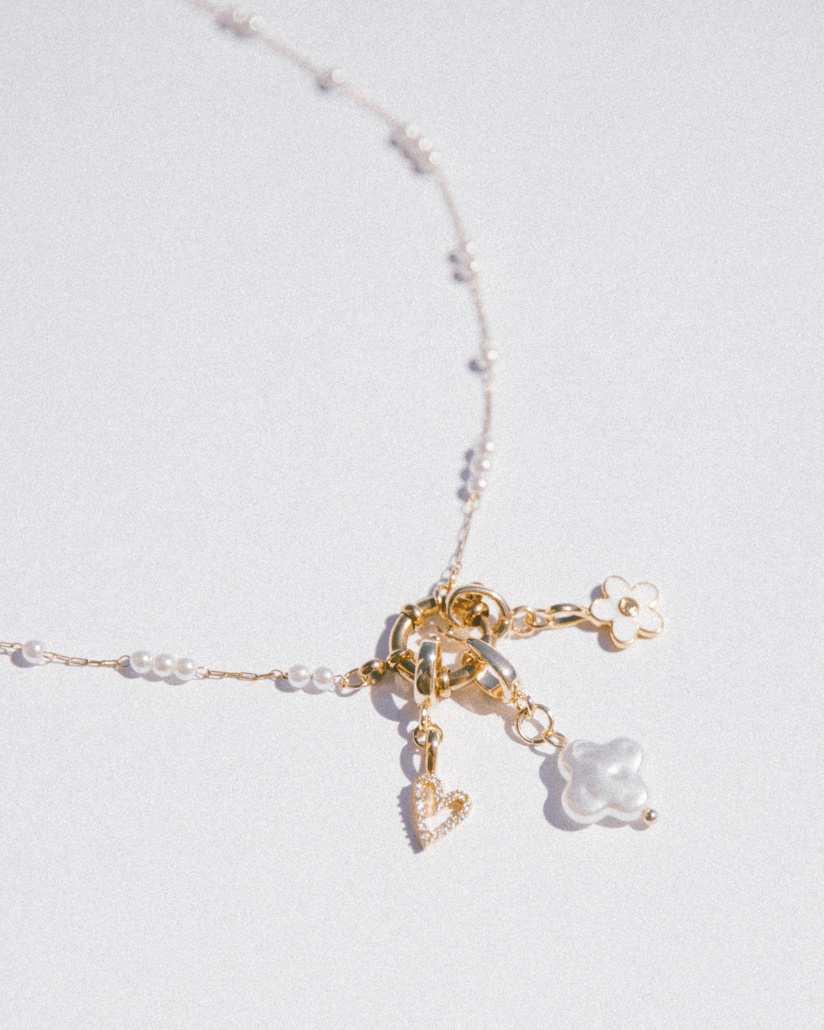 Necklace with gold and pearl charms on a light gray background