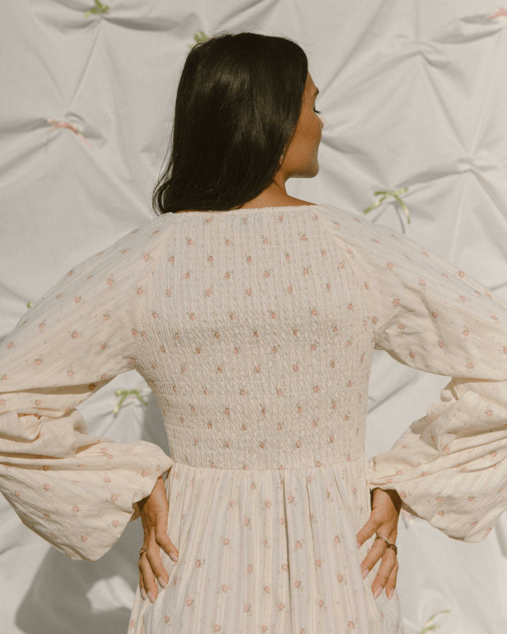 Woman showing the shirred elasticated back of long-sleeved feminine dress.