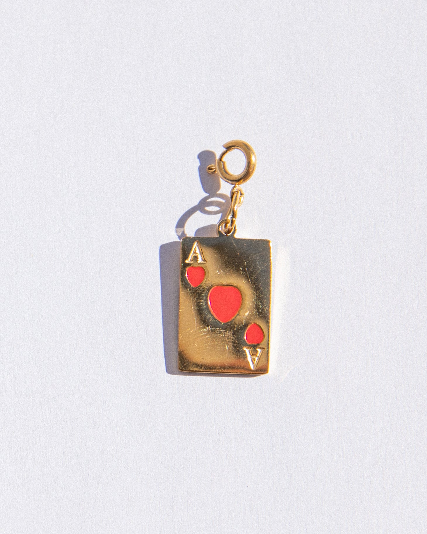 Gold pendant shaped like an Ace of Hearts card on a white background