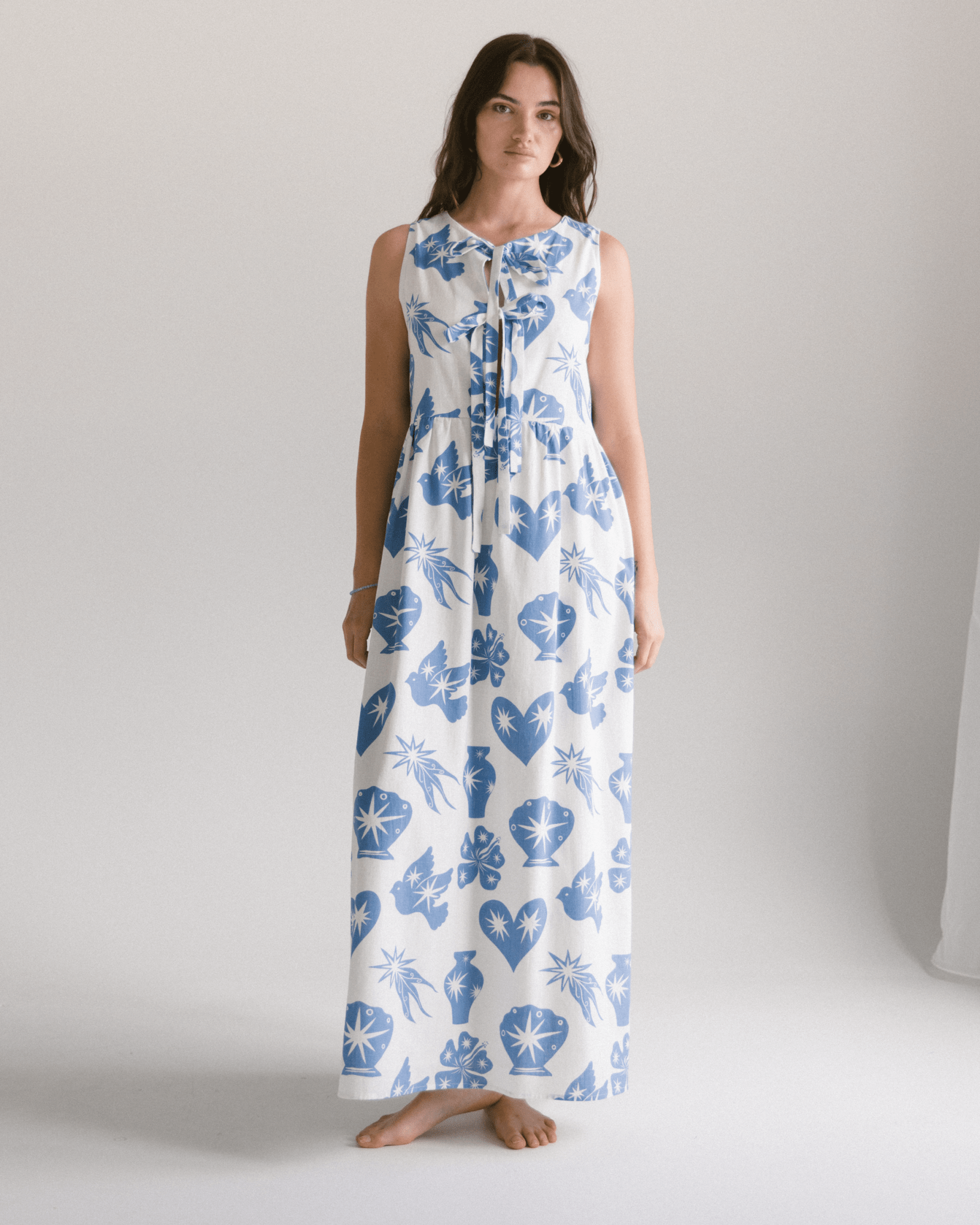 Woman wearing a long white dress with blue floral patterns on a plain background