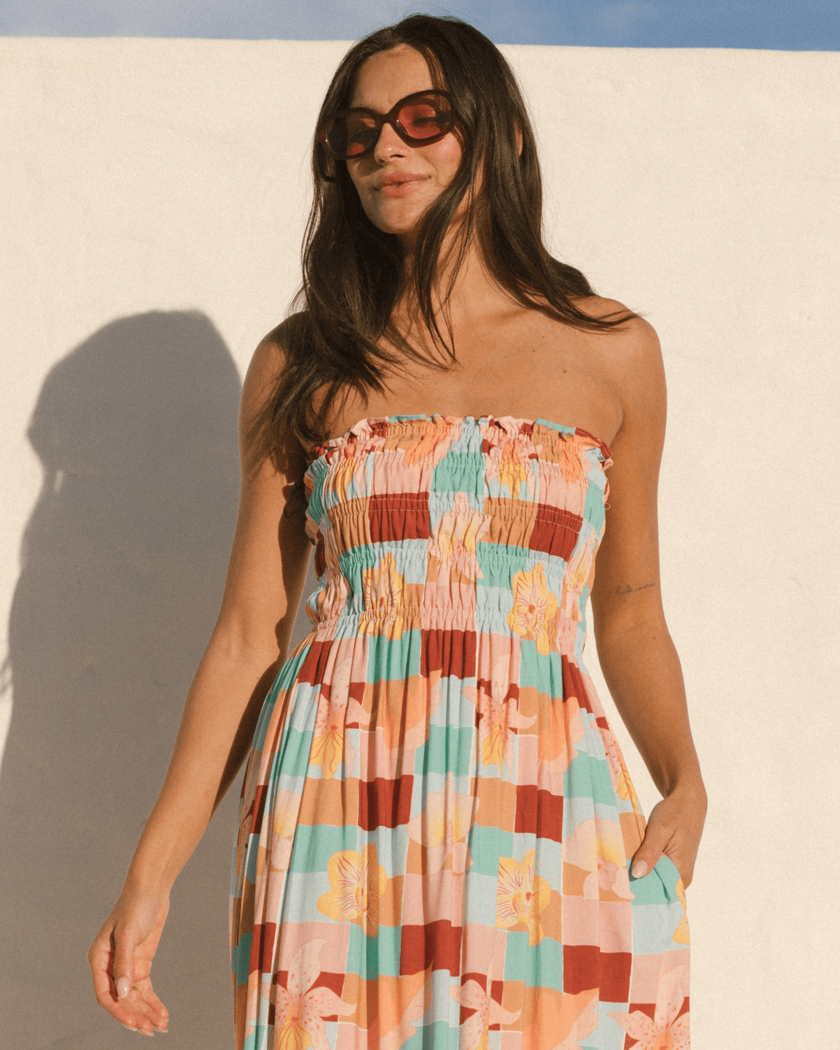Woman wearing a colorful strapless dress with pockets in the side-seam against a plain background