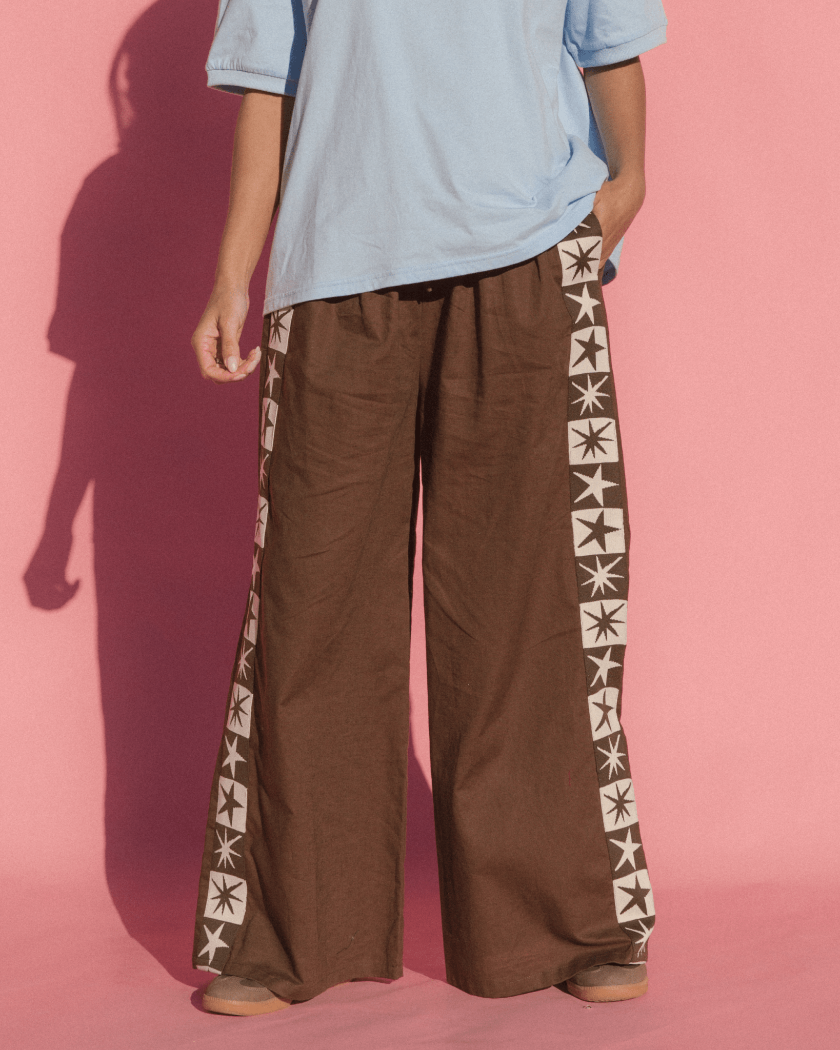 Person wearing brown wide-leg pants with star patterns on a pink background