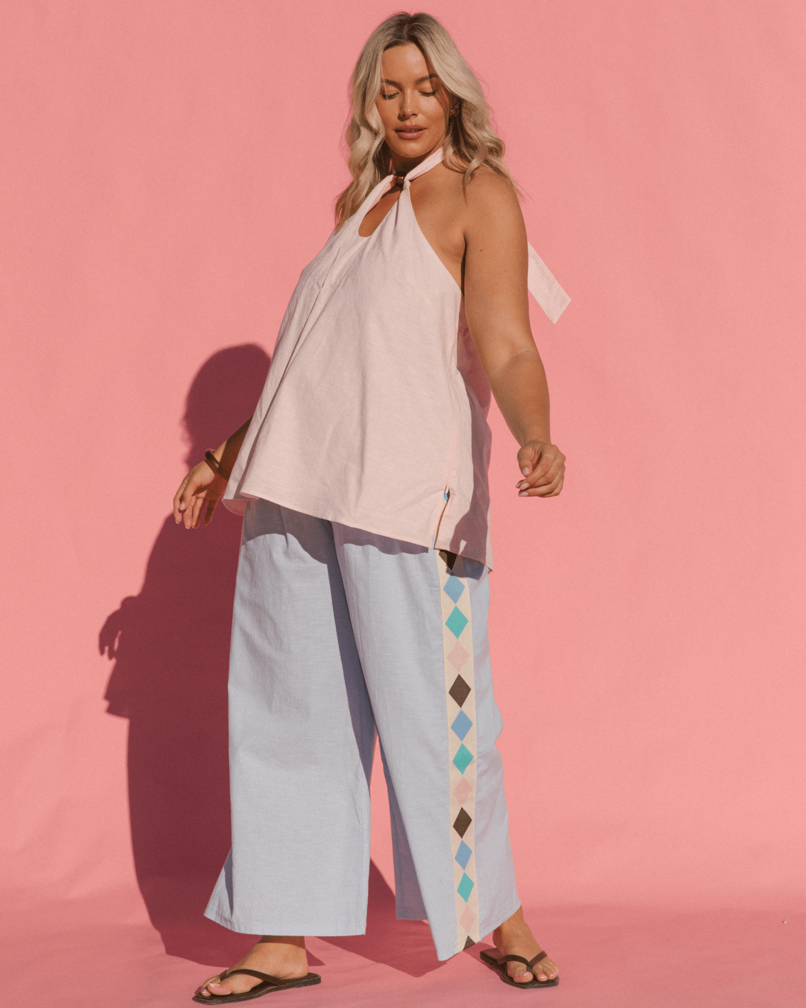 Woman wearing a light pink top and light blue pants with geometric patterns on a pink background