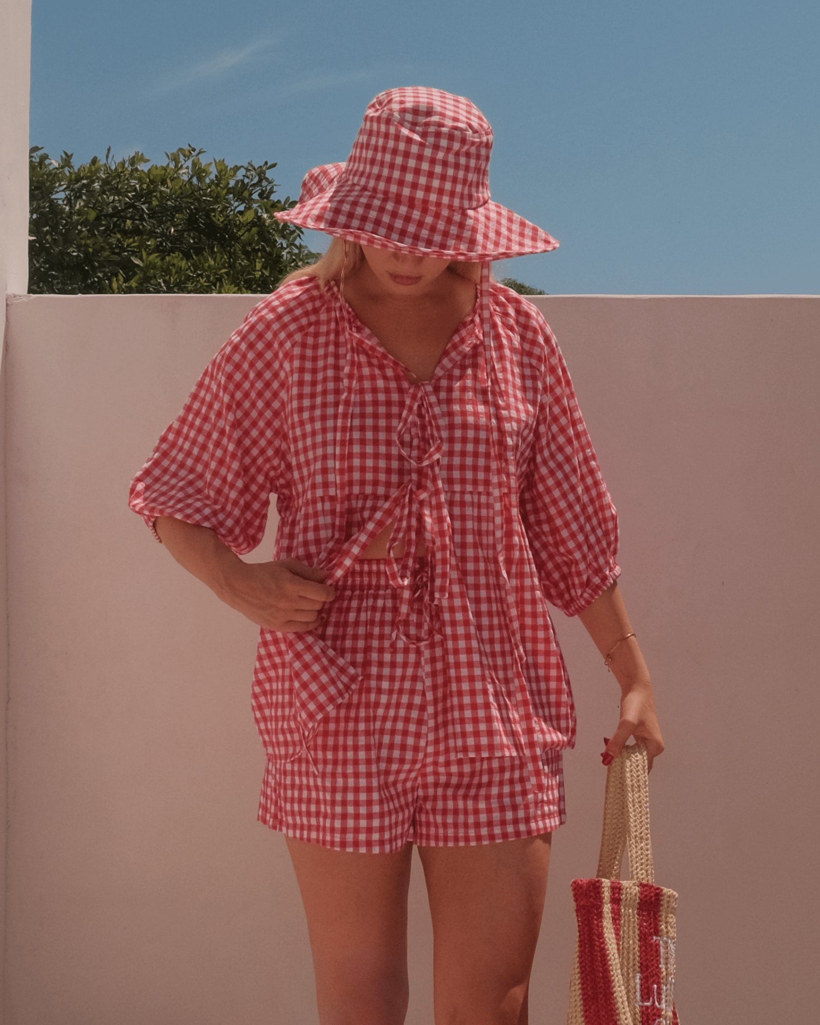 Woman wearing wide-brimmed red gingham hat with adjustable ties.