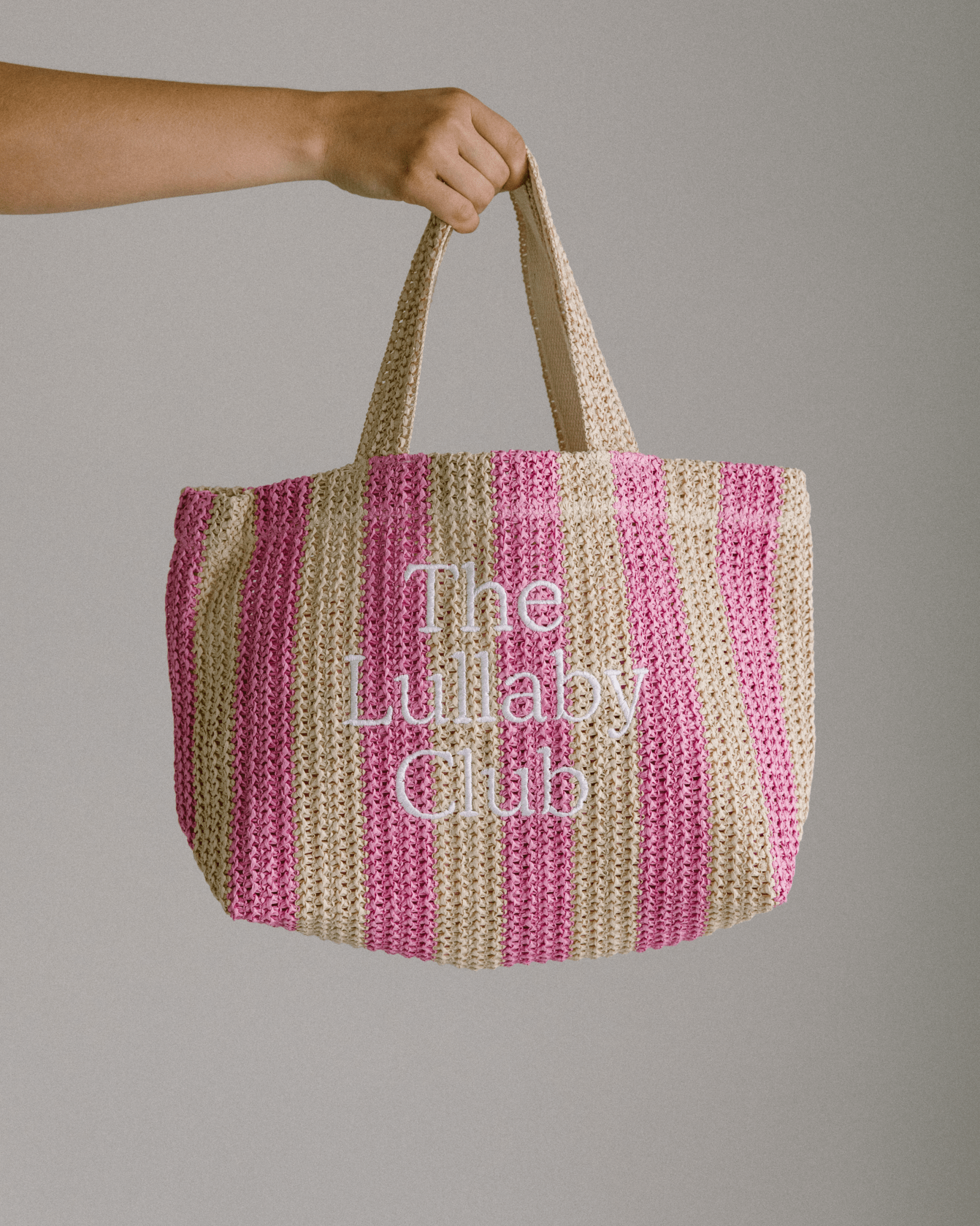 Striped pink & beige raffia holiday tote with 'The Lullaby Club' embroidered on the front.