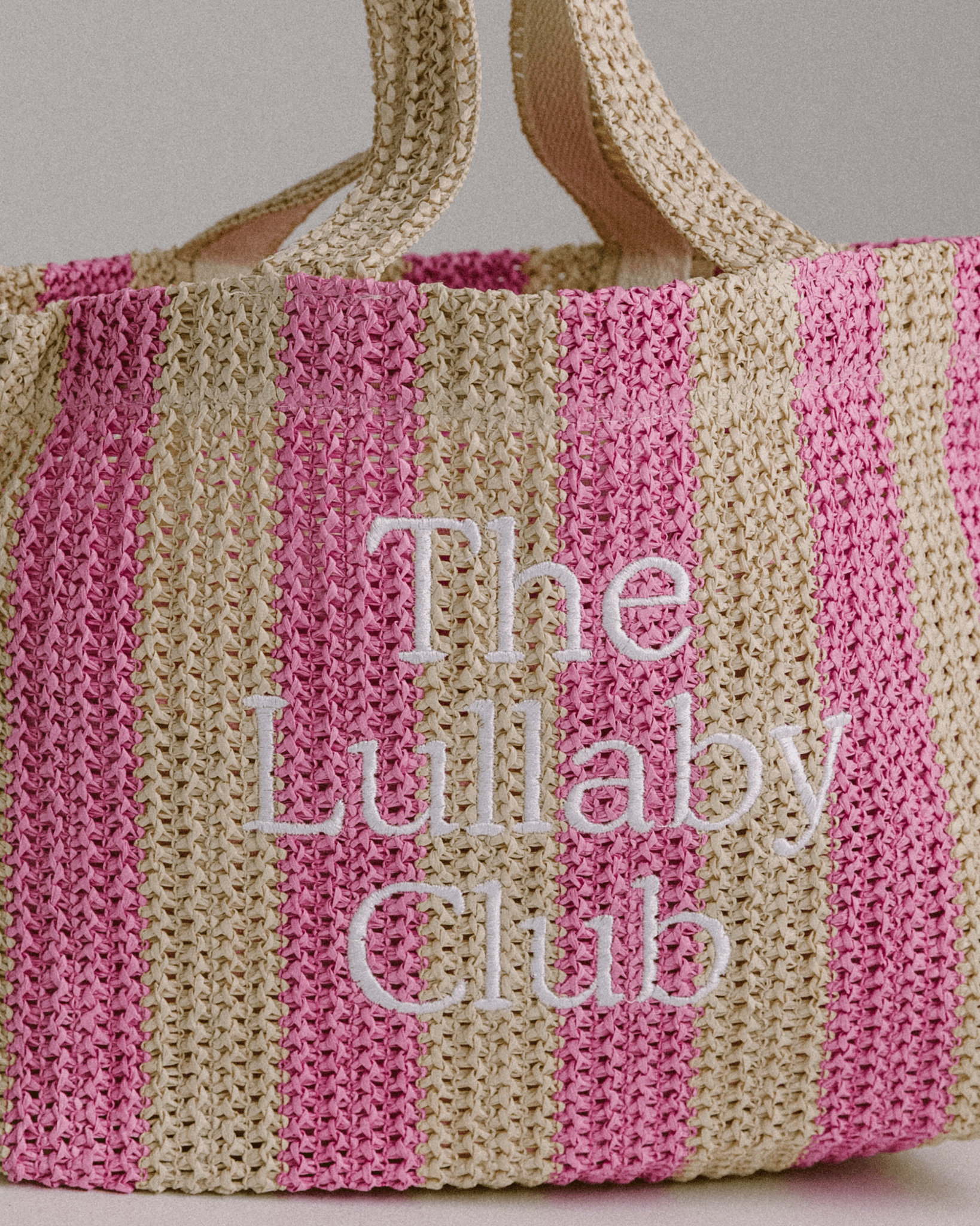 Up close detailing of embroidery of a pink & beige striped raffia tote bag.
