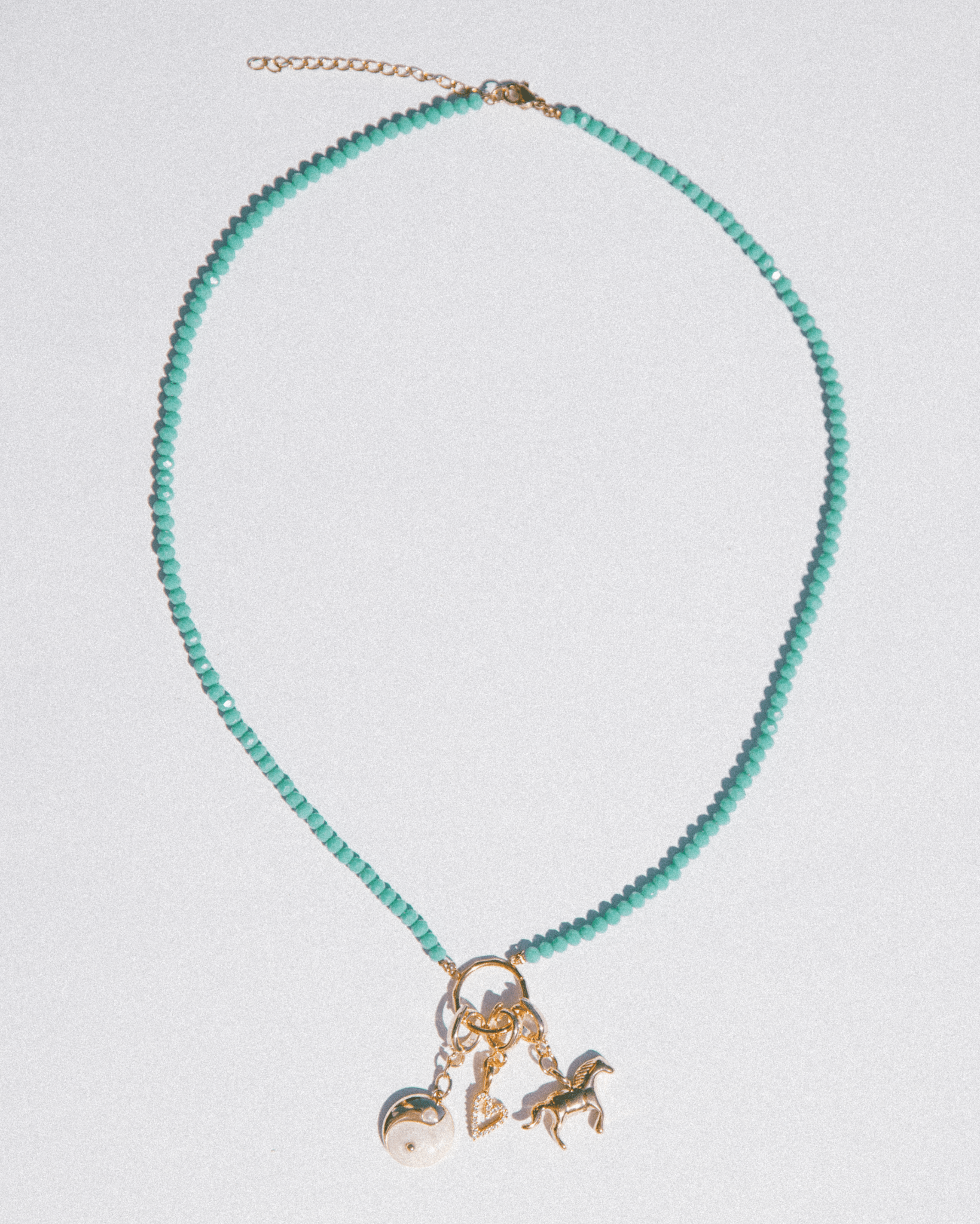 Turquoise beaded necklace with gold charm on a light gray background