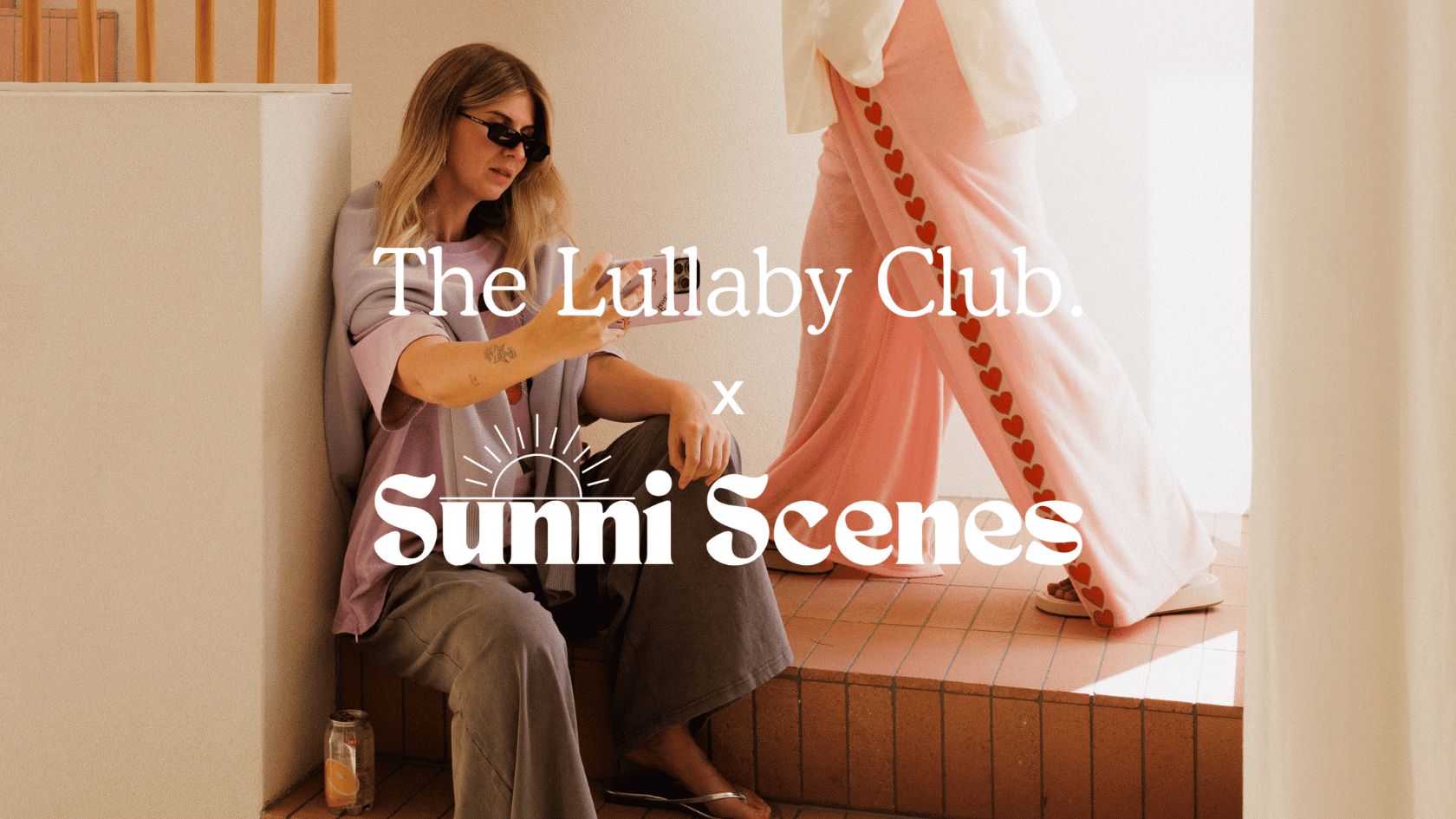 TLC x Sunni Scenes campaign image two women styled in the collection sitting and standing in a warm toned house location wearing the Darcy Knit Bomber and Essentials Pant in Love Story
