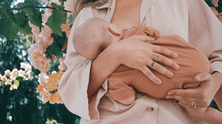 A mother feeding her baby in front of a bush of flowers