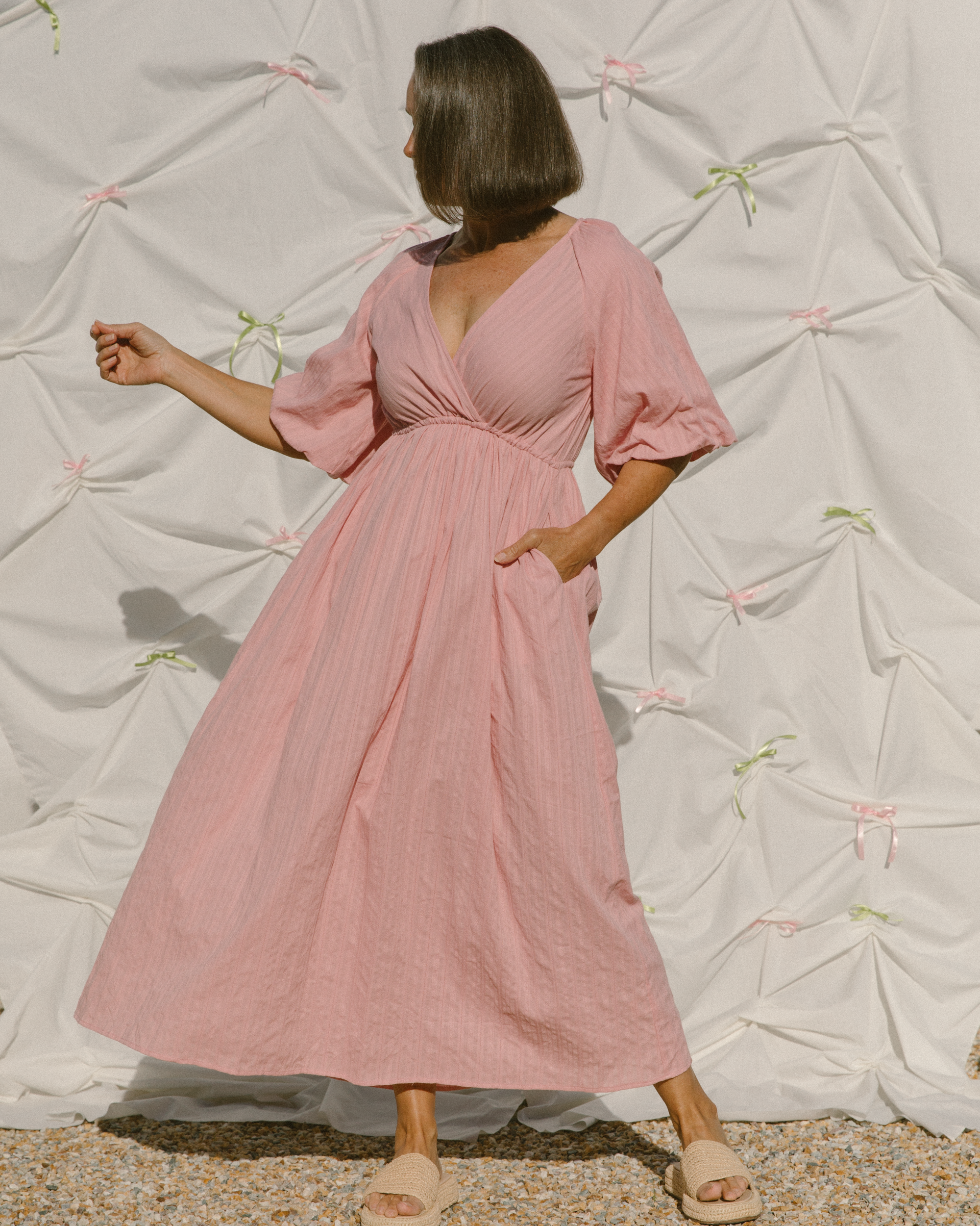 Woman wearing pink wrap style maxi dress with billowing sleeves. 