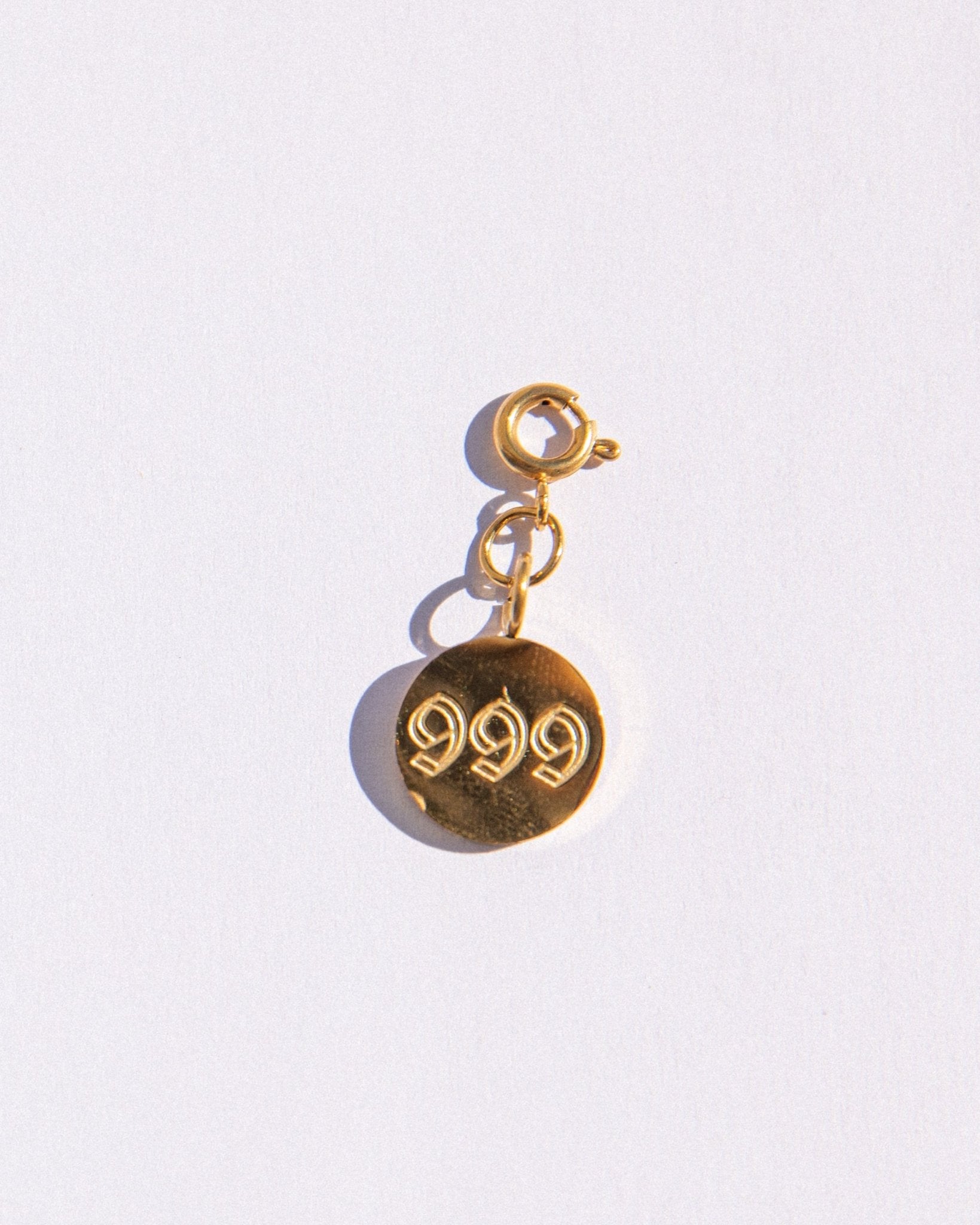 Circle gold charm with angel number '999' engraving on a white background