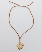 Gold flower pendant on a brown cord against a light gray background