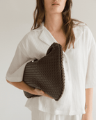 Woman holding a brown woven handbag against a plain background
