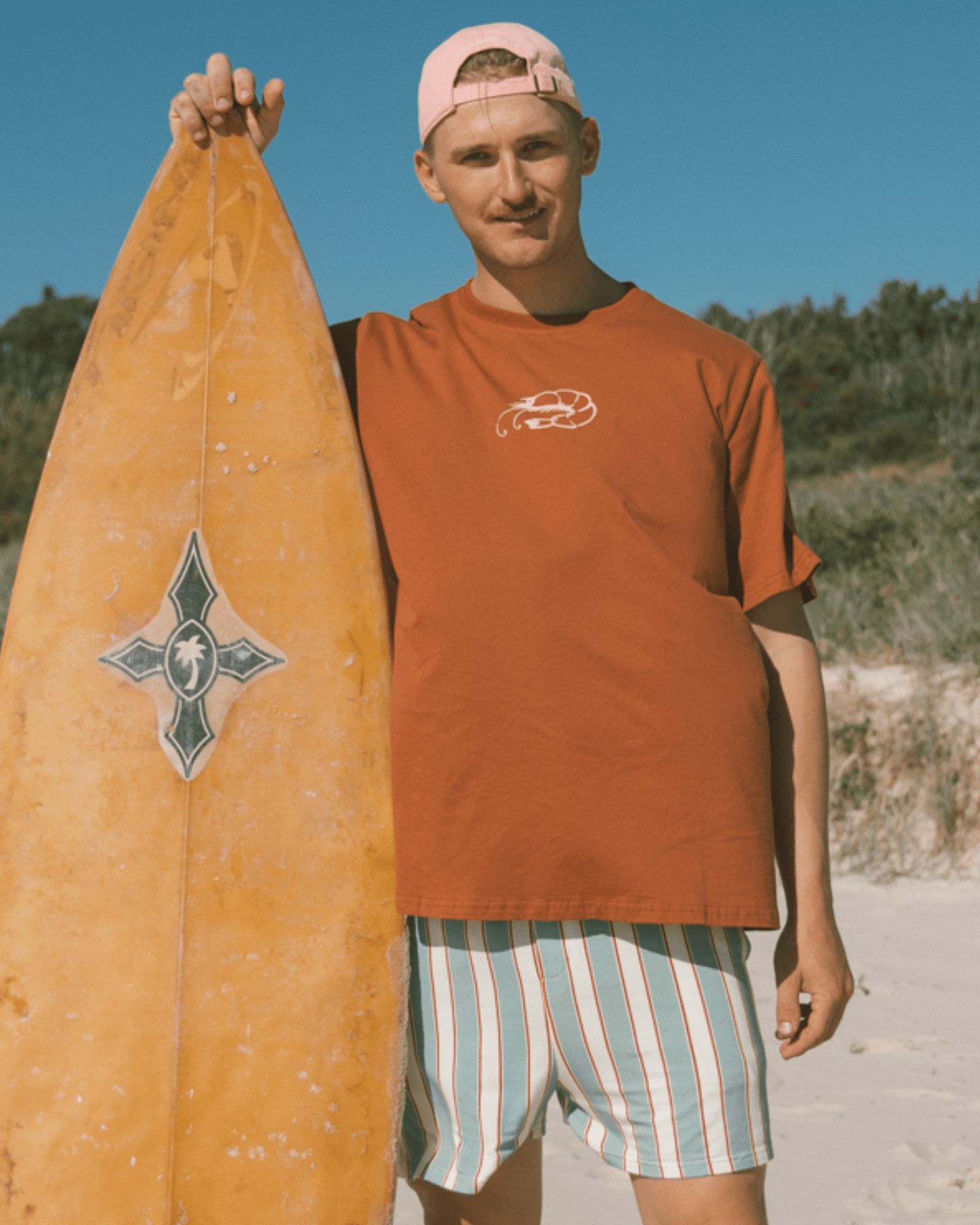 Man wearing rust pj shirt with prawn logo on front and matching striped pj boxer shorts.