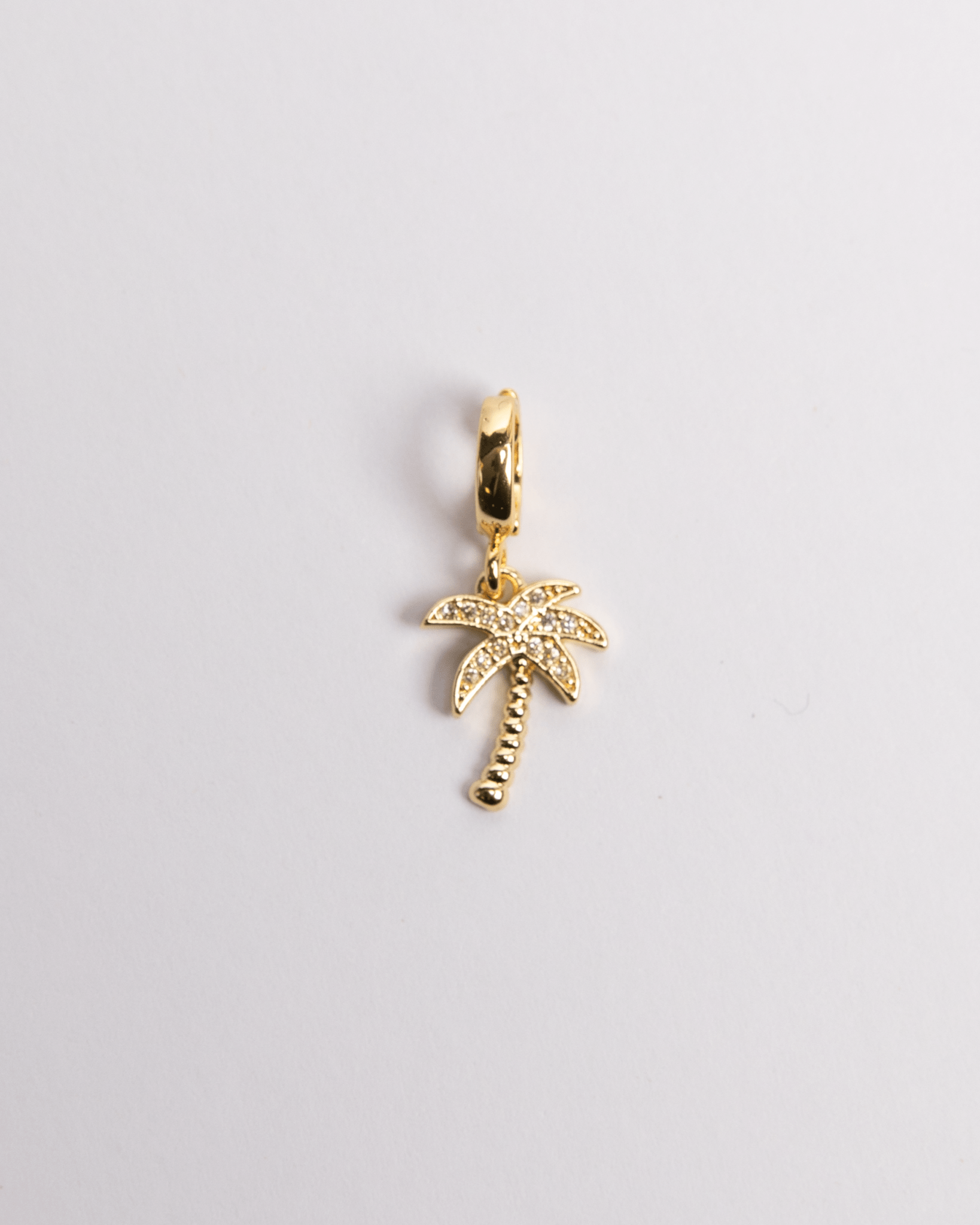 A gold-colored charm in the shape of a palm tree with a diamond pattern on the leaves.