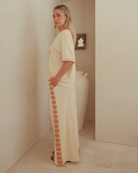 Woman wearing matching beige comfortable lounge set with pink & gold shells down the side-seams of pants.