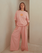 Woman wearing a light pink matching loungewear set with a oversized shirt and wide legged pants. 