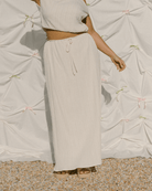 Woman wearing maxi length cream coloured skirt with drawstring waist.