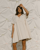 Woman wearing a summer mini dress in a light cream colour that has a wide-oversized deisng. 