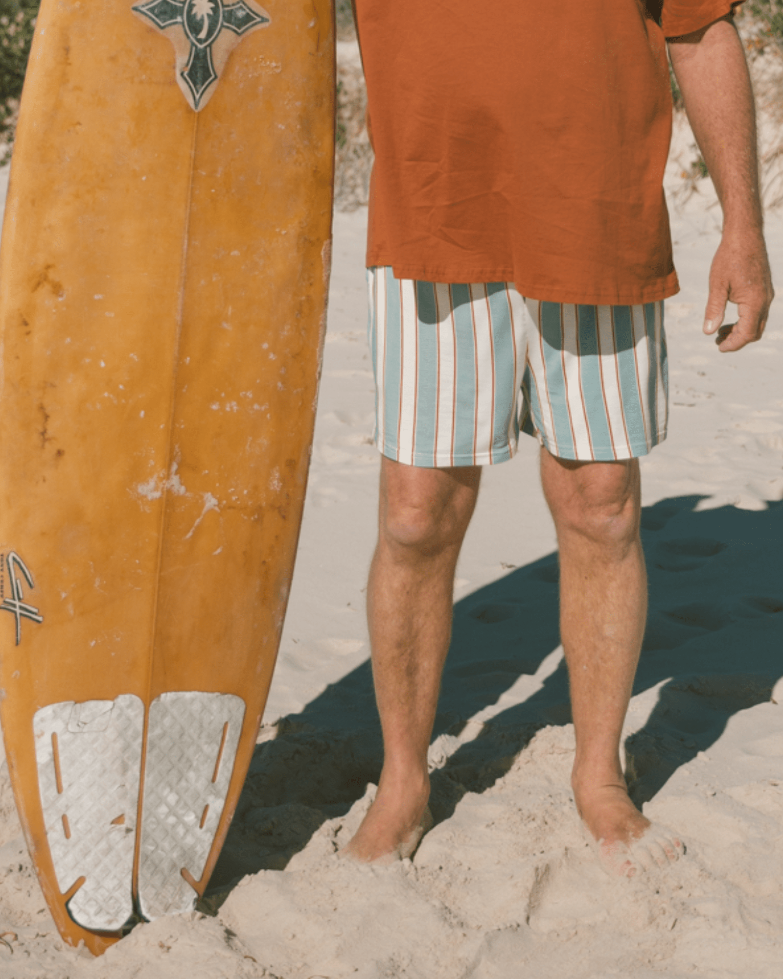 Person holding a yellow surfboard on a sandy beach