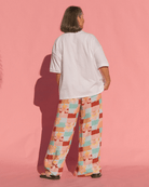 Person wearing a white t-shirt and colorful checkered pants on a pink background