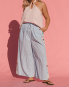Woman wearing a light pink top and light blue pants with floral patterns on a pink background