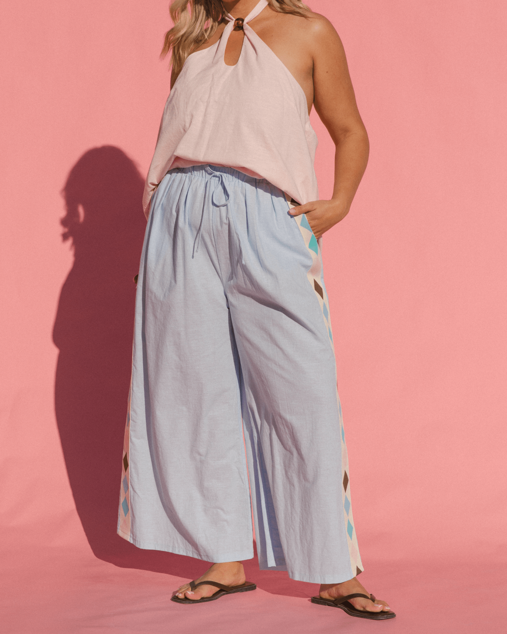 Woman wearing a light pink top and light blue pants with floral patterns on a pink background