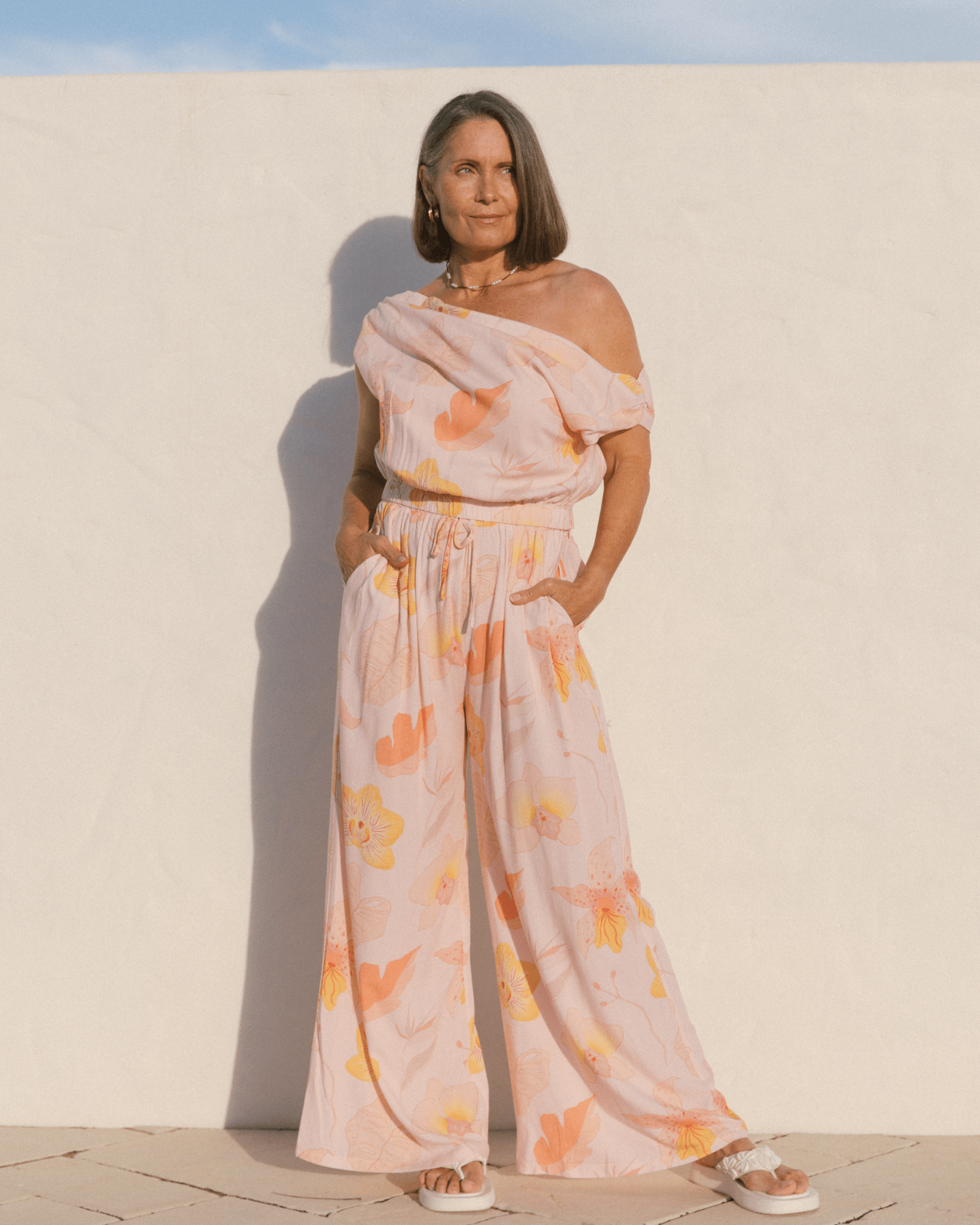 Woman wearing a spring floral matching set with off the shoulder crop top and long flowy pants. 