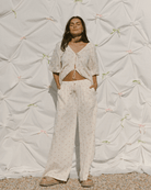 Woman wearing a light-colored outfit against a textured white wall.