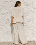 Woman wearing a light-colored outfit standing against a textured white wall.