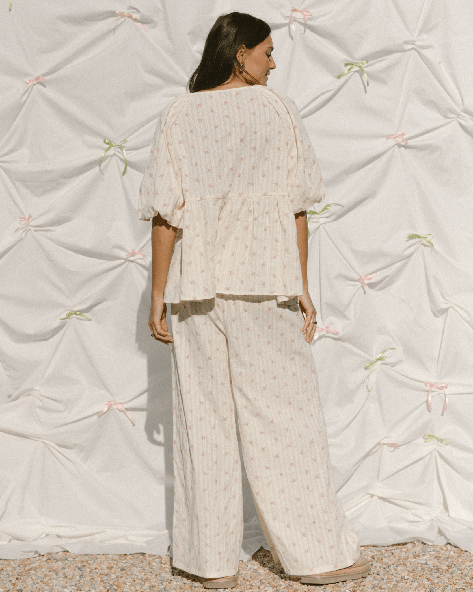 Woman wearing a light-colored outfit standing against a textured white wall.