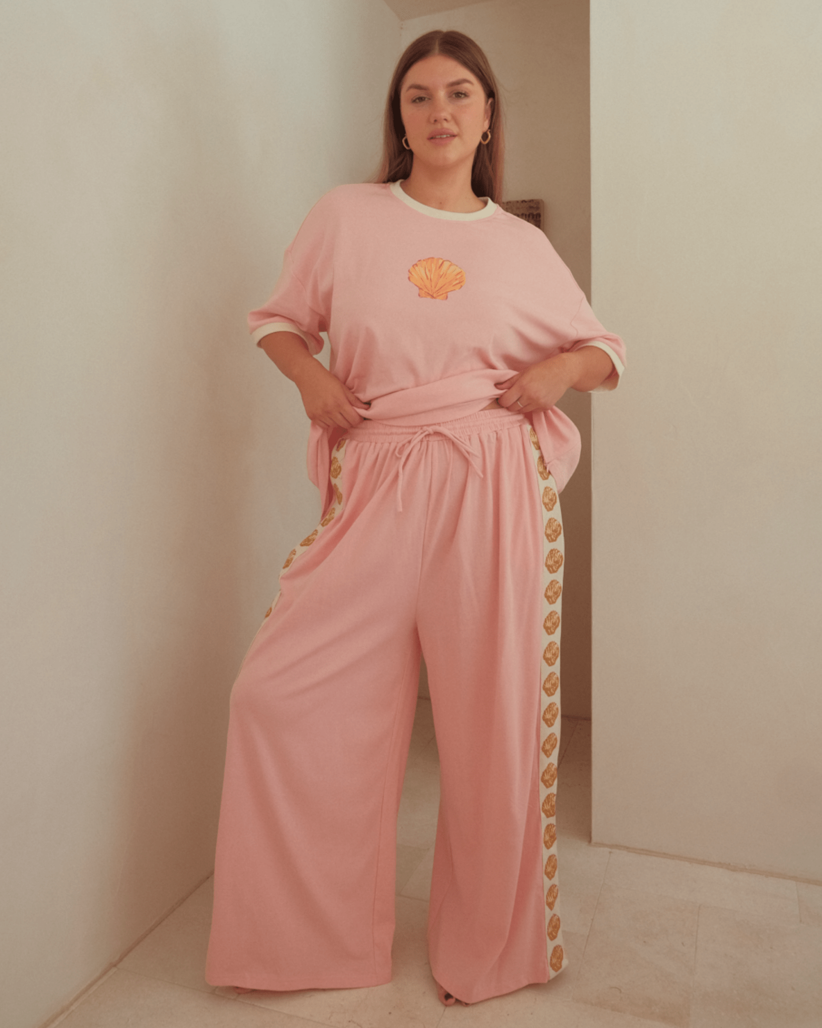 Woman wearing long breathable cotton pants in pink with golden shell detailing down the side. Showing the elastic, drawstring waistband.