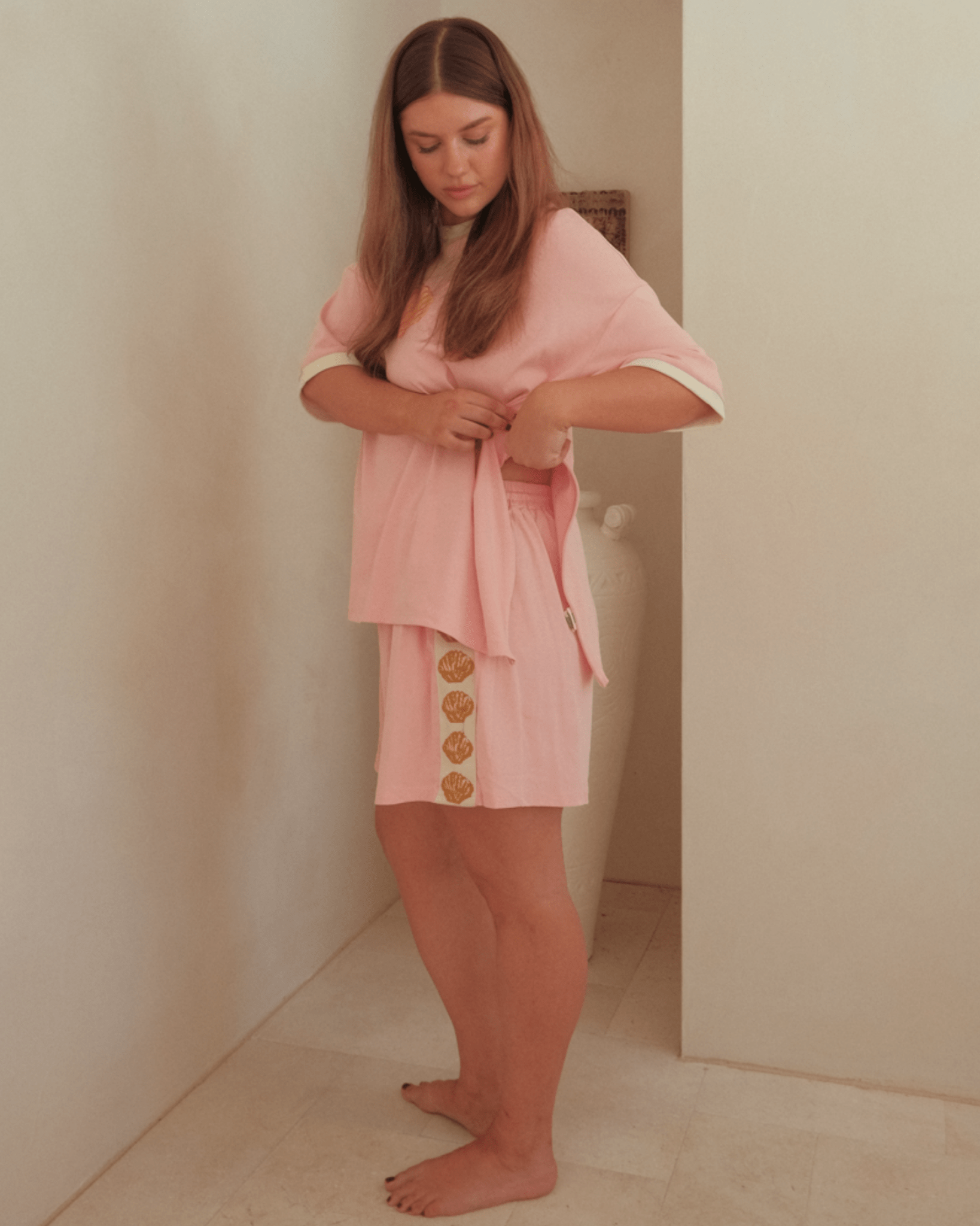 Woman wearing oversized pink loungewear set with gold shell detailing. Featuring breastfeeding side-seam zipper on the tshirt. 