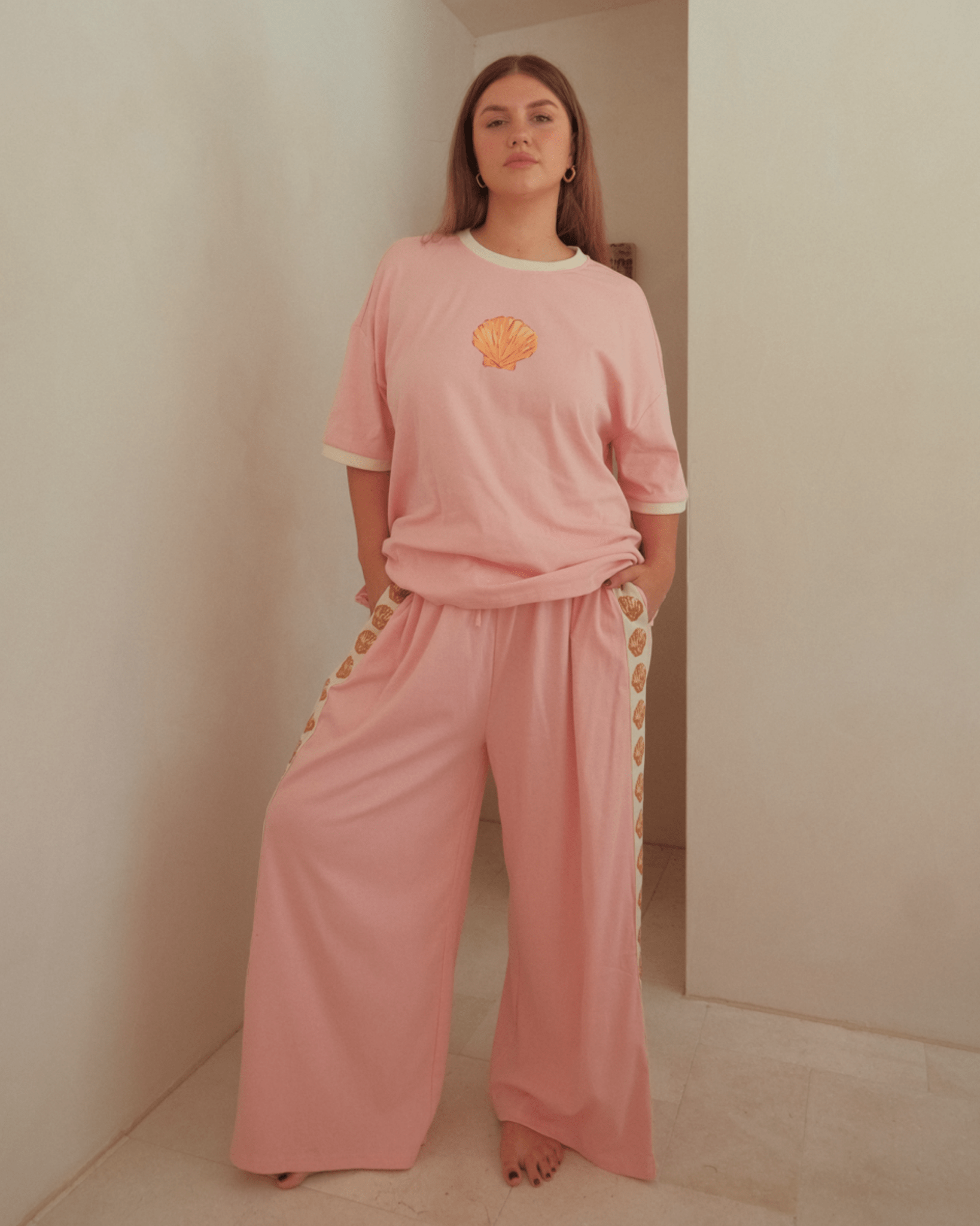 Woman wearing pink loungewear matching co-ord set. Featuring beachy style golden sell design and comfy fabric.