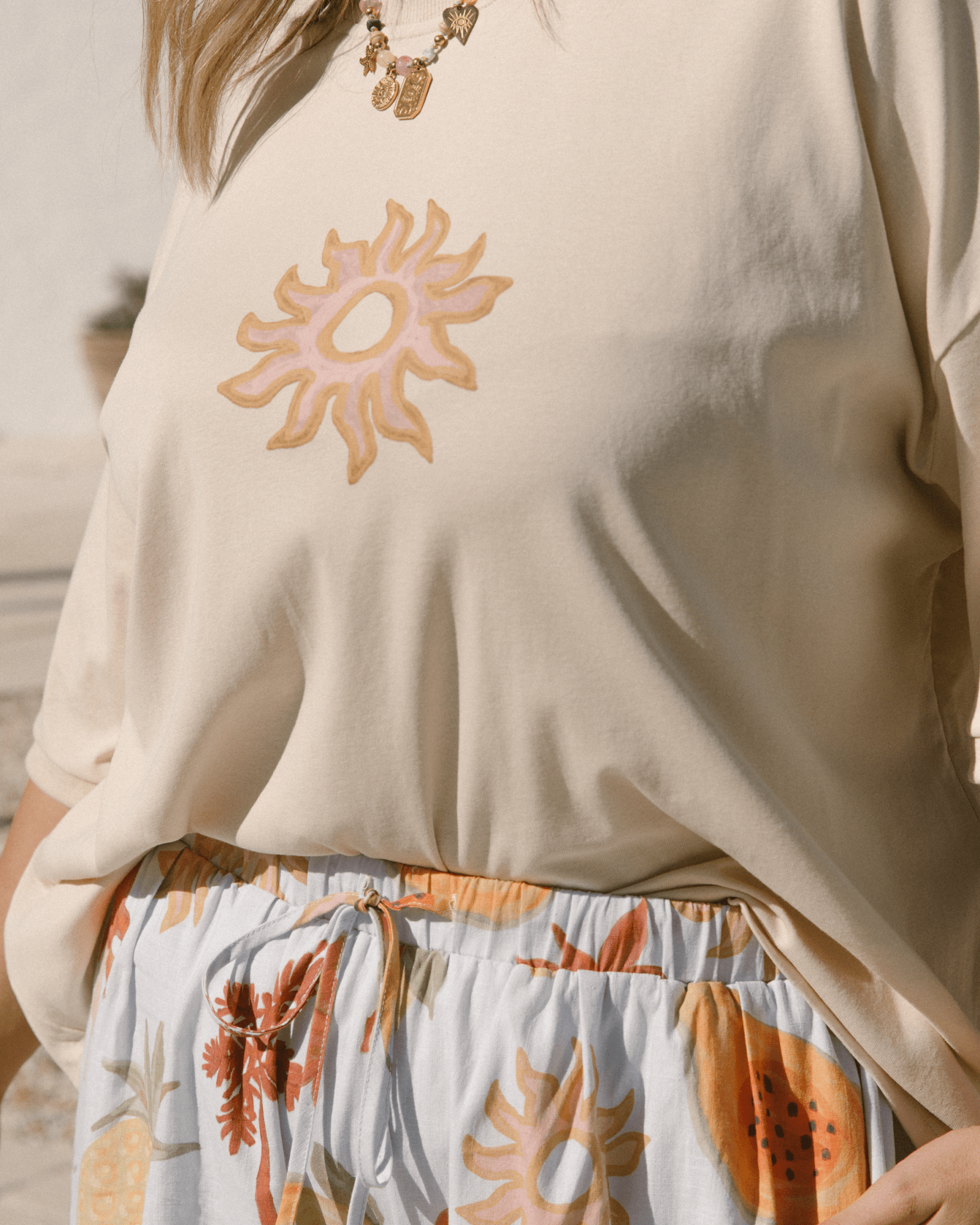 Beige oversized, wide tee with watercolour style sun graphic print & blue high waisted pants with summer pawpaw and pineapple floral print. 