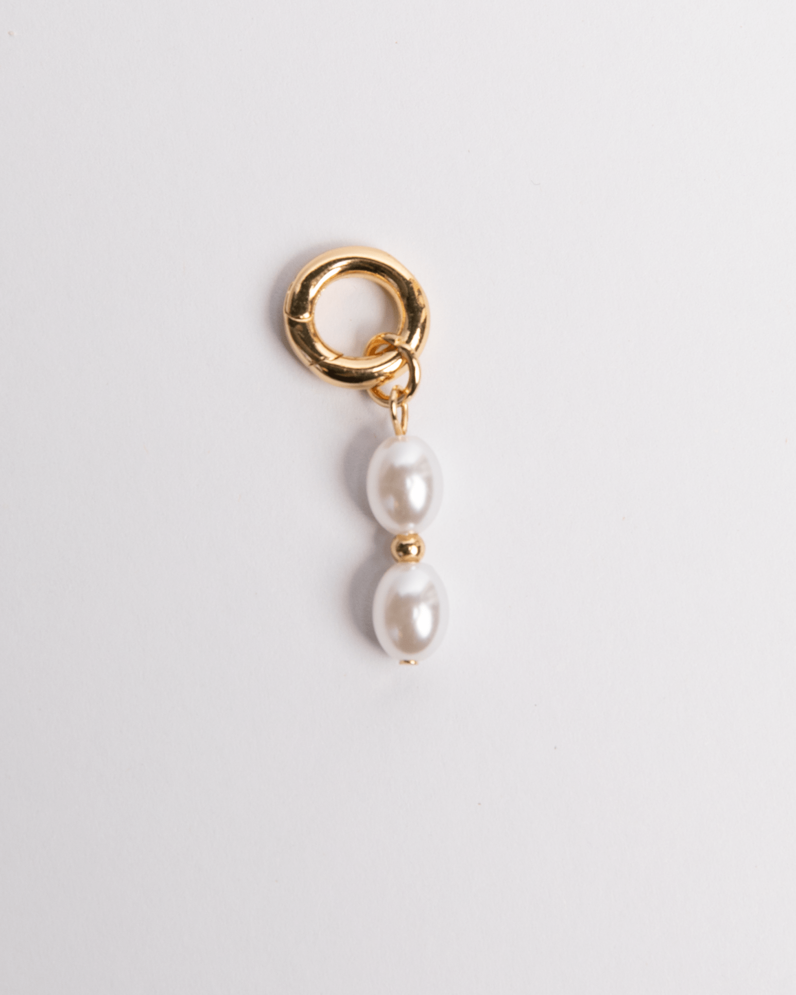 Gold charm with two pearls on a light gray background
