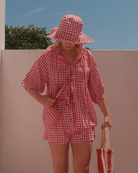 Woman wearing wide-brimmed red gingham hat with adjustable ties. 