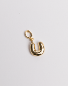 A gold-colored charm in the shape of the letter 'U' with a clasp on a white background.