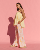 Woman wearing a light yellow top and floral pants against a pink background