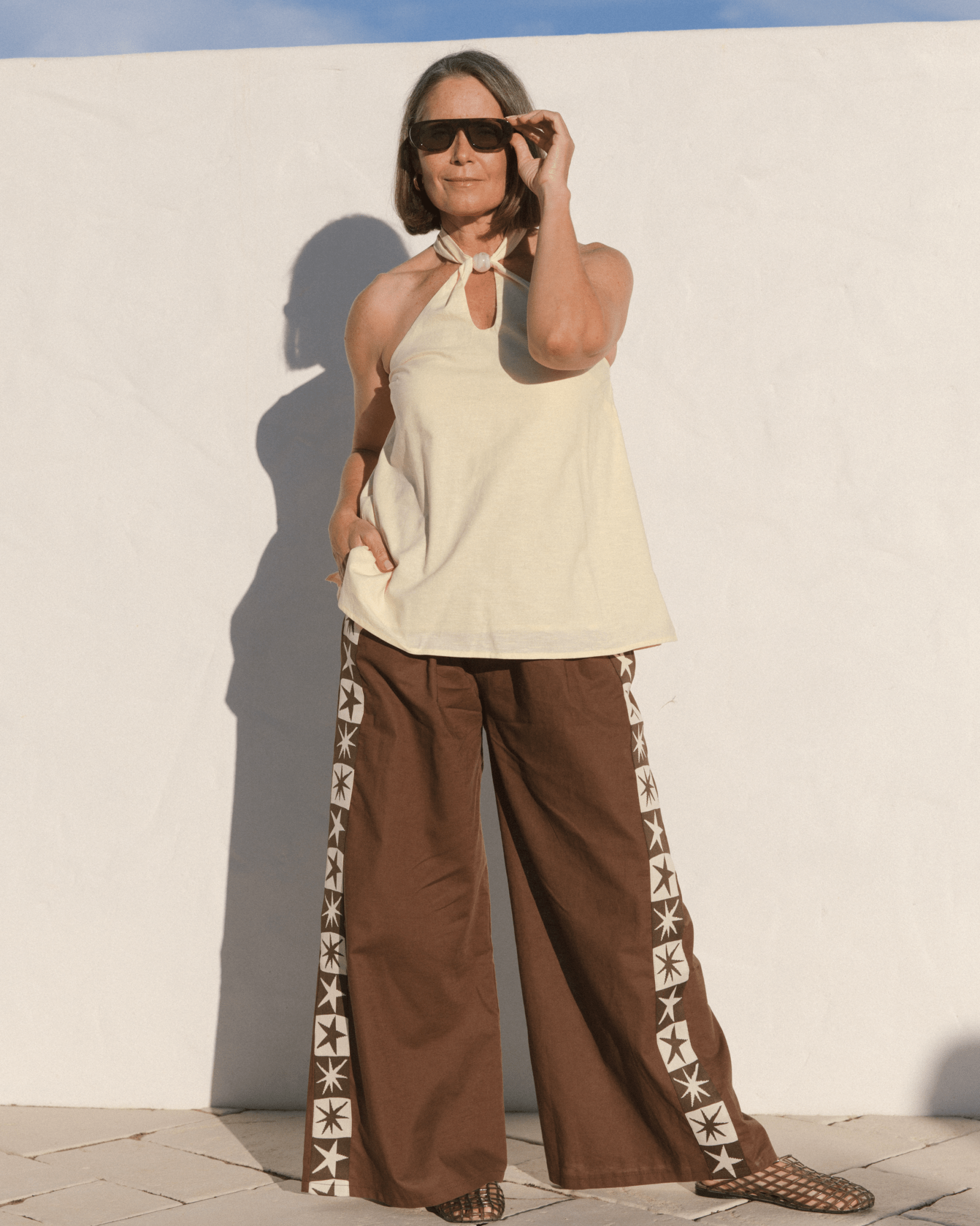 Women wearing butter yellow cotton halter top and brown linen pants with star detailing down the side. 